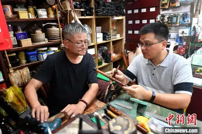 王道武(左)和儿子王增鑫讨论乐器工艺的改进和创新。　吕明 摄